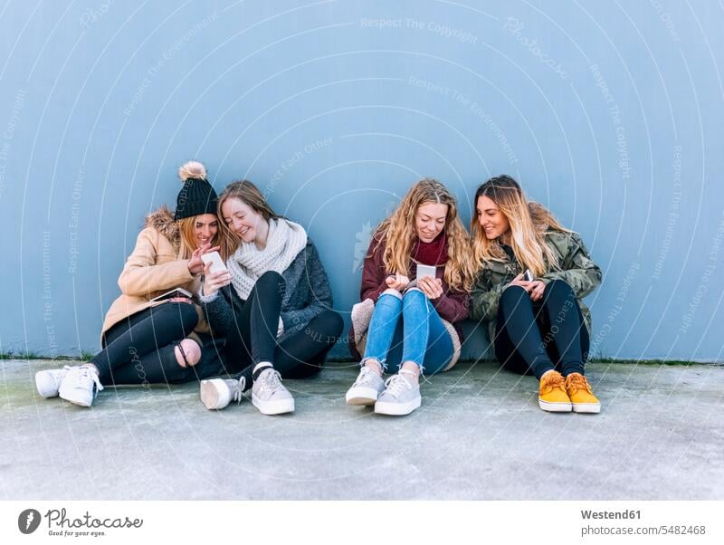 Vier Freunde sitzen nebeneinander auf dem Boden und schauen auf Mobiltelefone Freundinnen benutzen benützen Smartphone iPhone Smartphones Freundschaft