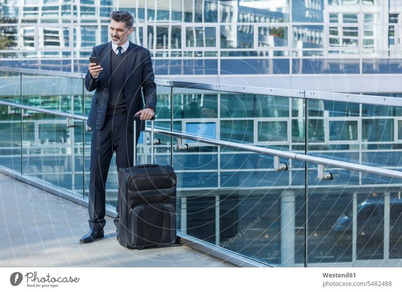Geschäftsmann mit Handy stehend mit Koffer auf der Brücke steht Businessmann Businessmänner Geschäftsmänner Geschäftsreise Geschaeftsreise Geschäftsreisen
