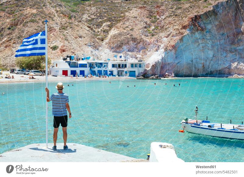 Griechenland, Milos, Firopotamos Beach, Mann schaut aufs Meer, hält sich an griechischer Flagge fest Tourist Touristen Männer männlich Strand Straende Strände