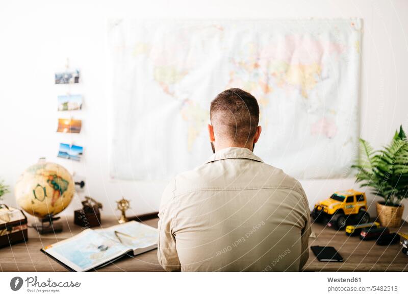 Junger Reisender plant seine nächste Reise von zu Hause aus sitzen sitzend sitzt Schreibtisch Arbeitstisch Schreibtische Fernweh Reiselust reisen Travel