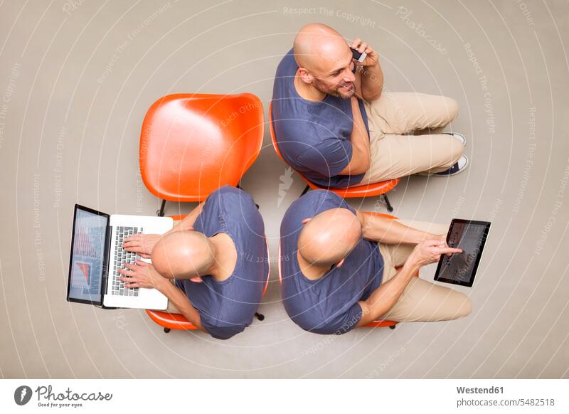 Mann sitzt auf Stühlen mit tragbaren Geräten, Multitasking Online Soziale Medien Social Media teilen aufteilen Smartphone iPhone Smartphones telefonieren