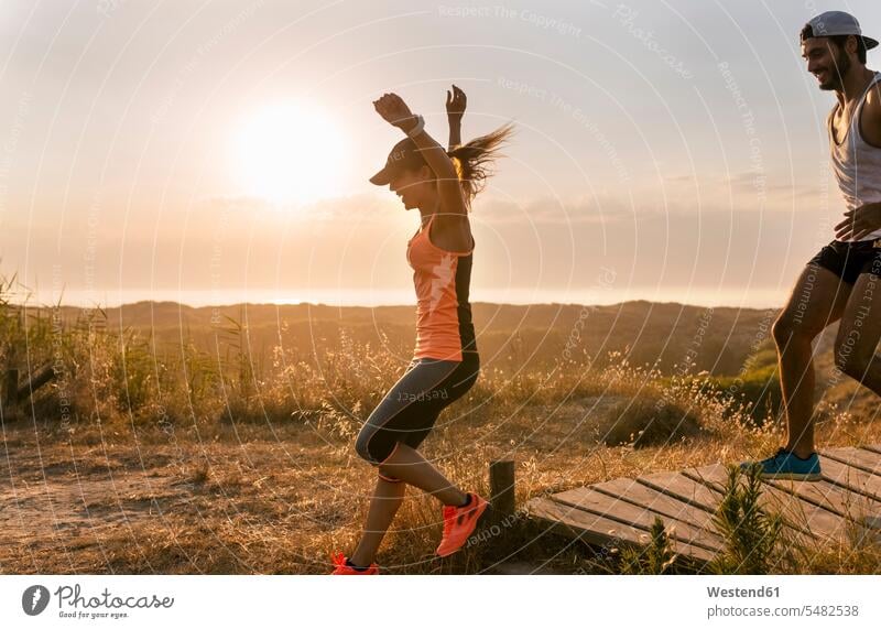 Spanien, Aviles, Athletenpaar läuft bei Sonnenuntergang einen Küstenweg entlang Paar Pärchen Paare Partnerschaft Läuferin Laeuferinnen Läuferinnen Abend abends