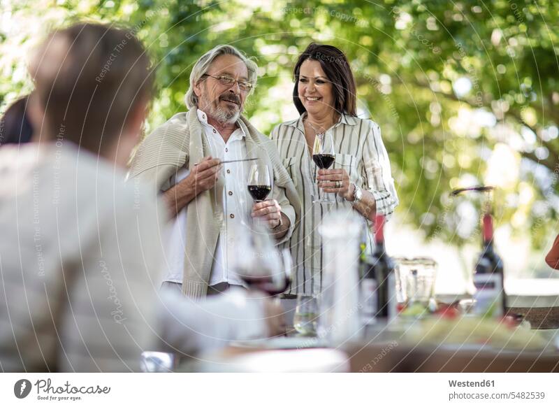Älteres Ehepaar, das während des Familienmittagessens im Garten einen Toast ausbringt feiern Rotwein Rotweine Gruppe Gruppe von Menschen Menschengruppe Wein