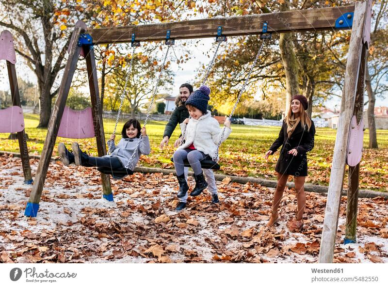 Glückliche Familie hat im Herbst Spaß an Schaukeln Familien Mensch Menschen Leute People Personen Park Parkanlagen Parks schaukeln schwingen Freizeitkleidung