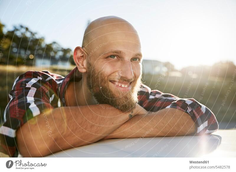 Porträt eines kahlköpfigen jungen Mannes mit Bart, der sich auf dem Autodach abstützt Männer männlich Portrait Porträts Portraits Erwachsener erwachsen Mensch