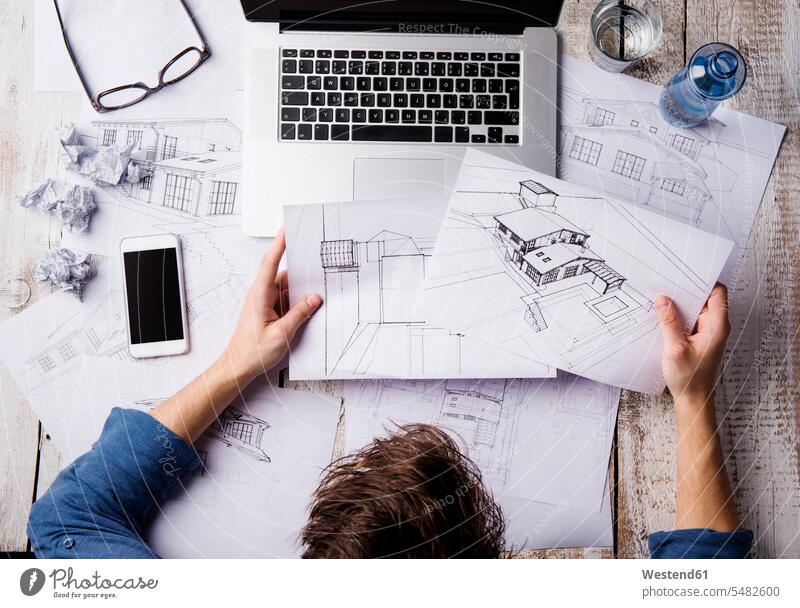 Architekt arbeitet am Schreibtisch mit Laptop und betrachtet Skizzen sitzen sitzend sitzt entwerfen Entwurf Notebook Laptops Notebooks arbeiten Arbeit Mann