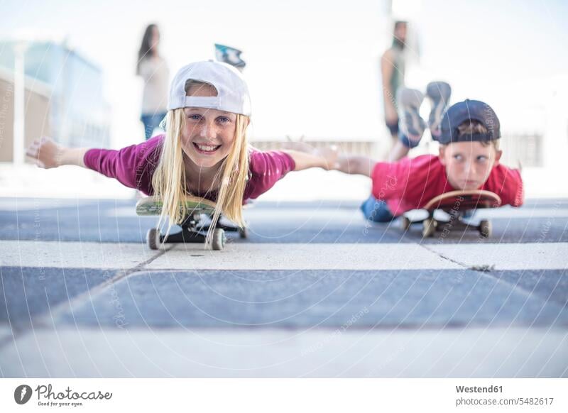 Kinder skateboarden auf der Straße, auf dem Bauch liegend Skateboard Rollbretter Skateboards Skateboarder Skateboardfahrer Skateboarders Skater lachen Mädchen