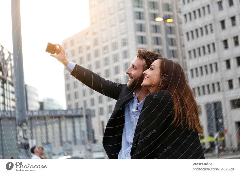 Lächelnder junger Geschäftsmann und Geschäftsfrau nehmen Selfie im Freien Businessmann Businessmänner Geschäftsmänner Selfies lächeln Geschäftsfrauen