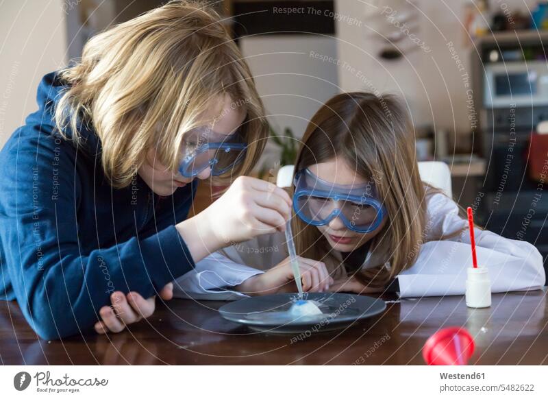 Zwei Kinder tragen eine Schutzbrille und benutzen zu Hause ein Chemie-Set Experiment experimentieren Chemiebaukasten Versuch Pipette Pipetten betrachten