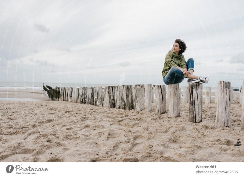 Frau sitzt auf Holzpfahl am Strand weiblich Frauen Beach Straende Strände Beaches sitzen sitzend Erwachsener erwachsen Mensch Menschen Leute People Personen