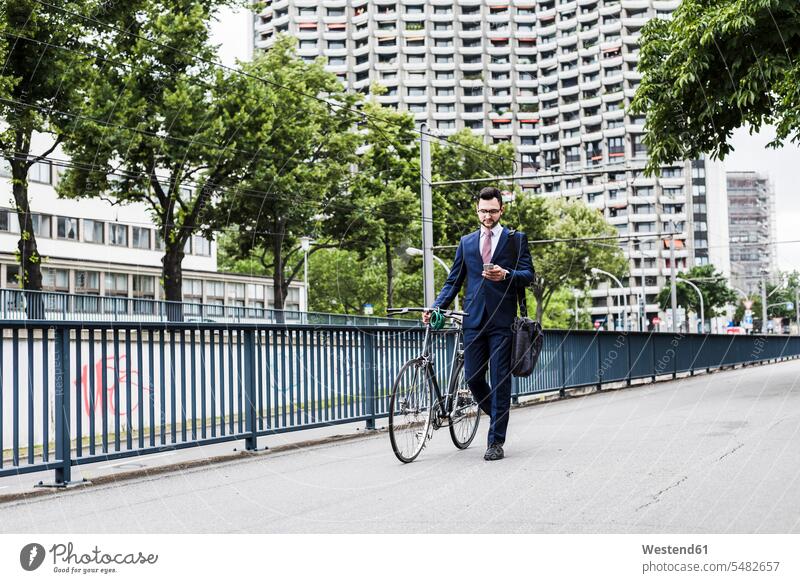Geschäftsmann mit Fahrrad zu Fuß in der Stadt, mit Smartphone Bikes Fahrräder Räder Rad schieben anschieben gehen gehend geht SMS Textnachricht Handy