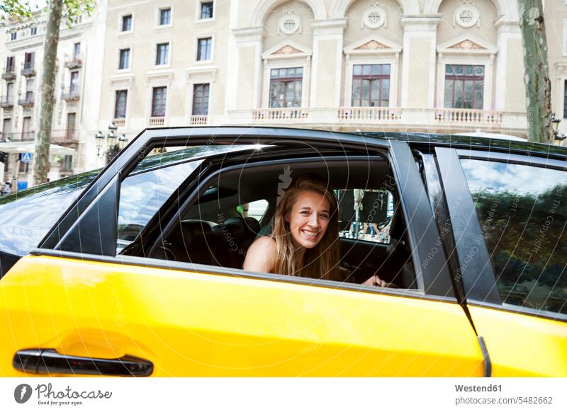 Spanien, Barcelona, glückliche junge Frau, die aus dem Taxifenster schaut Taxis Taxen weiblich Frauen Auto Wagen PKWs Automobil Autos Kraftfahrzeug