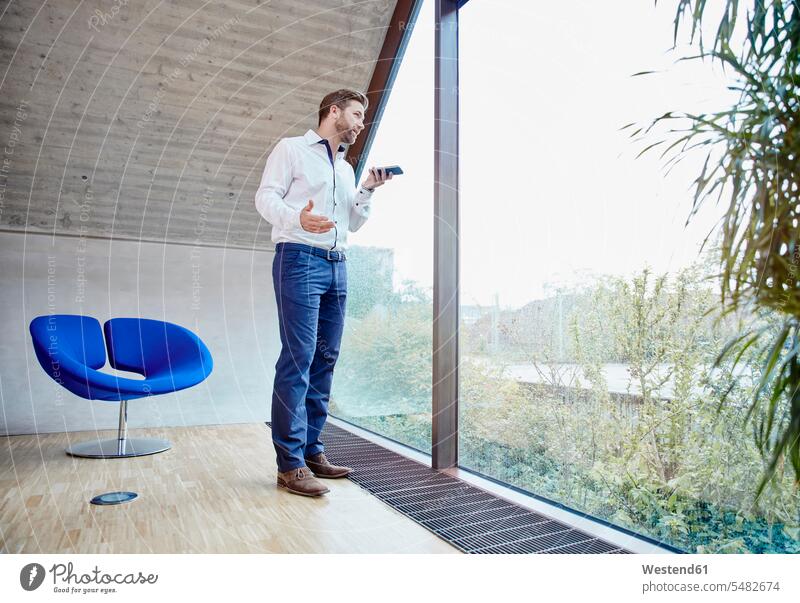 Geschäftsmann benutzt Handy im Dachbodenbüro am Fenster Mobiltelefon Handies Handys Mobiltelefone telefonieren anrufen Anruf telephonieren stehen stehend steht