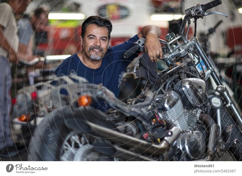 Porträt eines lächelnden Mechanikers in der Motorradwerkstatt Motorräder Monteur arbeiten Arbeit reparieren Reparatur Kraftfahrzeug Verkehrsmittel KFZ Industrie