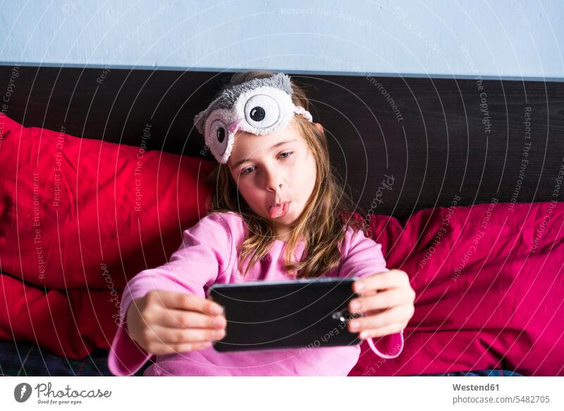 Mädchen auf dem Bett liegend nimmt Selfie mit Handy Smartphone iPhone Smartphones Selfies weiblich Mobiltelefon Handies Handys Mobiltelefone Kind Kinder Kids