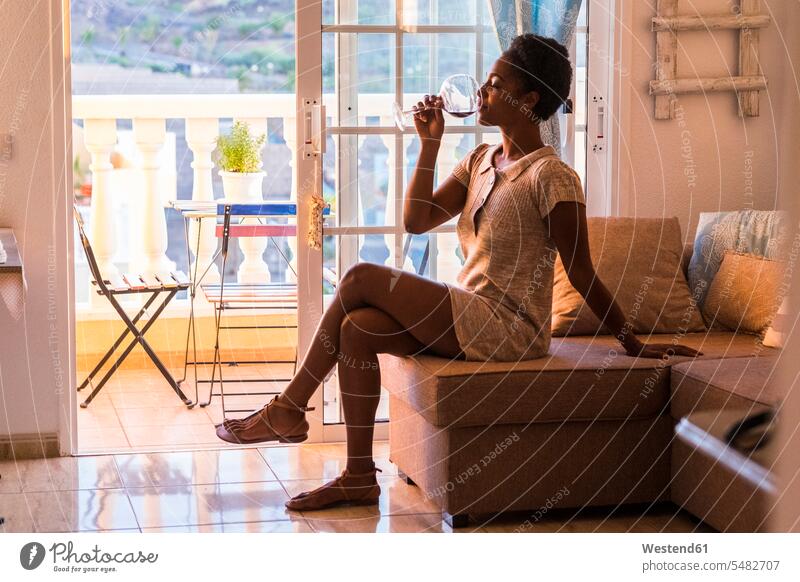 Junge Frau sitzt auf der Couch und trinkt ein Glas Rotwein weiblich Frauen sitzen sitzend Erwachsener erwachsen Mensch Menschen Leute People Personen Wohnzimmer