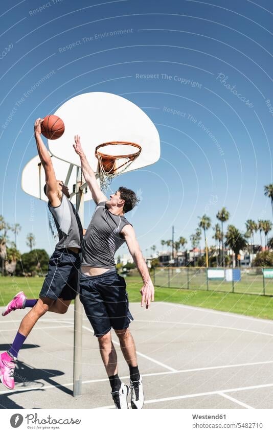 Zwei junge Männer spielen Basketball auf einem Aussenplatz Freizeitaktivität Hobby Hobbies Hand heben Bewegung sich bewegen Korb Vitalität Elan Schwung