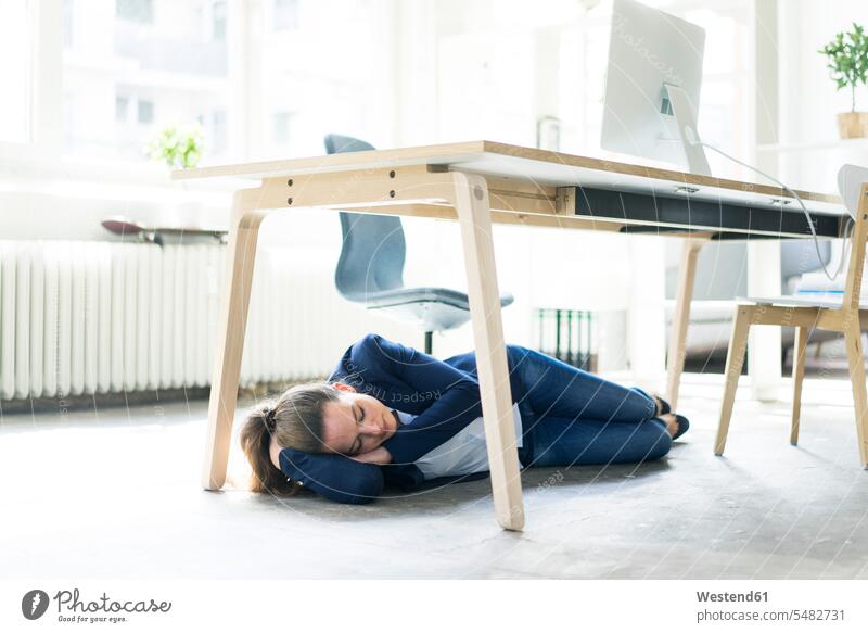 Geschäftsfrau, die im Büro unter dem Tisch liegt und schläft liegen liegend Geschäftsfrauen Businesswomen Businessfrauen Businesswoman schlafen schlafend Frau