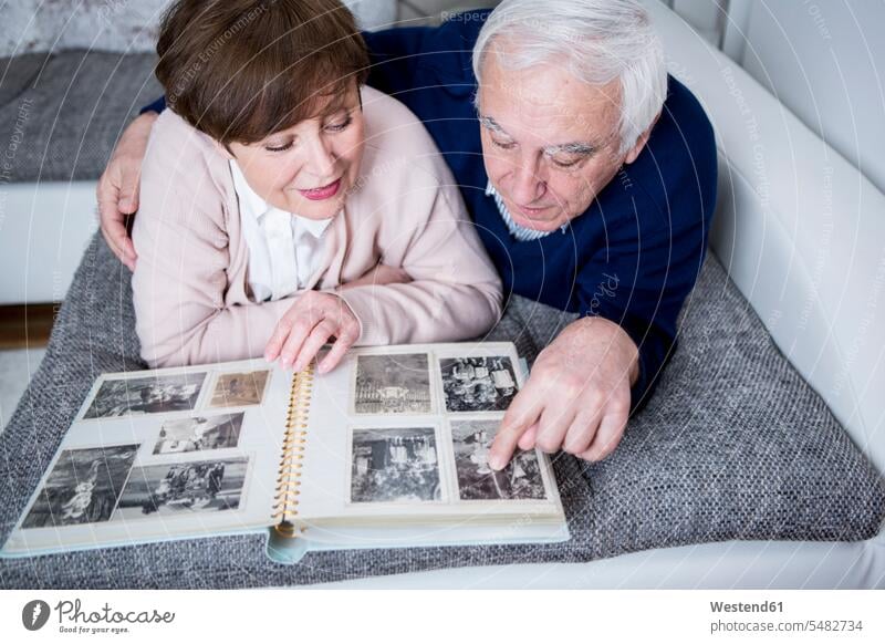Älteres Ehepaar liegt auf dem Sofa und schaut sich ein Fotoalbum an Fotos ansehen Senioren alte ältere Fotoalben betrachten betrachtend liegen liegend Paar