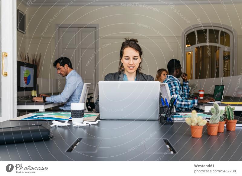 Junge Geschäftsfrau mit Laptop, Kollegen arbeiten im Hintergrund Team sitzen sitzend sitzt Arbeit Notebook Laptops Notebooks Geschäftsfrauen Businesswomen