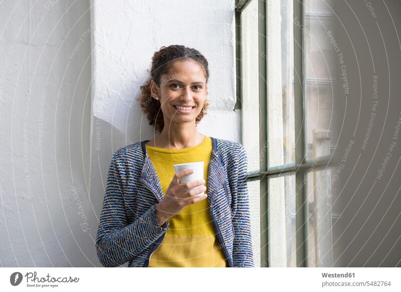 Junge Frau steht am Fenster mit einer Tasse Kaffee Kaffeetasse Kaffeetassen trinken weiblich Frauen Getränk Getraenk Getränke Getraenke Food and Drink