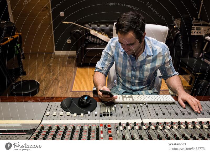 Mann im Kontrollraum eines Tonstudios mit Blick auf Handy Mischpult Aufnahmestudio Tontechniker Männer männlich Erwachsener erwachsen Mensch Menschen Leute