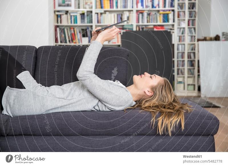 Junge Frau liegt auf Couch und benutzt digitales Tablett schön Freude freuen lächeln Freizeitkleidung casual Freizeitbekleidung dunkelblond dunkelblondes Haar
