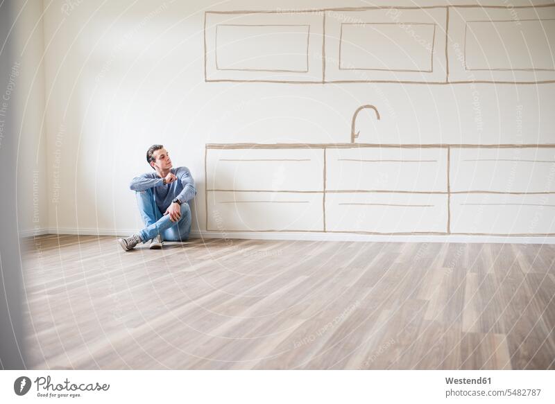 Junger Mann in neuer Wohnung sitzt auf dem Boden und denkt über Innenarchitektur nach wohnen Wohnungen sitzen sitzend Männer männlich Wohnen Erwachsener