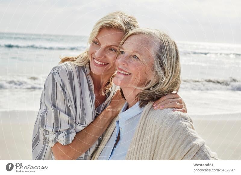 Ältere Frau und ihre erwachsene Tochter stehen am Strand und umarmen Beach Straende Strände Beaches Mutter Mami Mutti Mütter Mama stehend steht Töchter