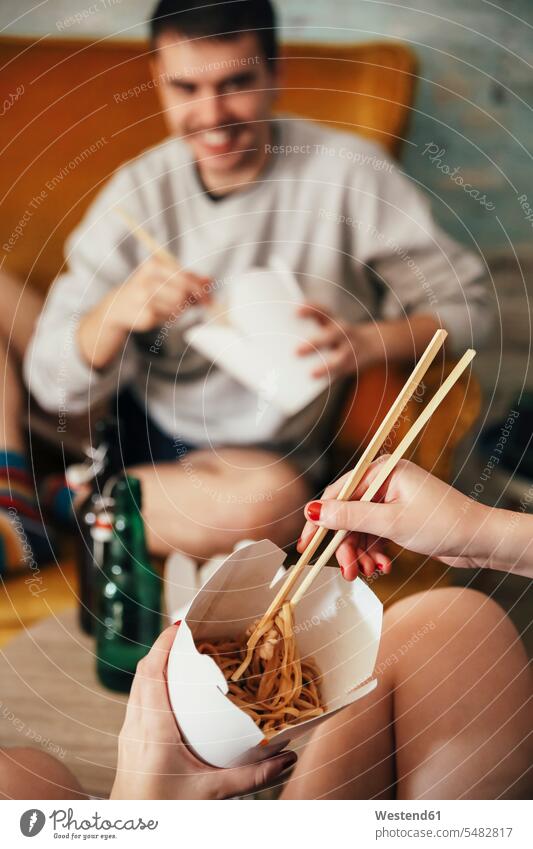 Junges Paar isst zu Hause chinesisches Essen zum Mitnehmen Box Boxen offenes Lächeln lachen offenes Laecheln Stäbchen Essstäbchen Esstäbchen Esstaebchen