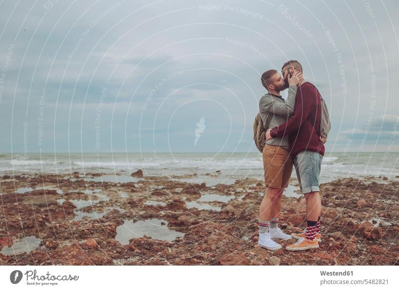 Junges schwules Paar küsst sich am Strand Pärchen Paare Partnerschaft küssen Küsse Kuss Beach Straende Strände Beaches Mensch Menschen Leute People Personen