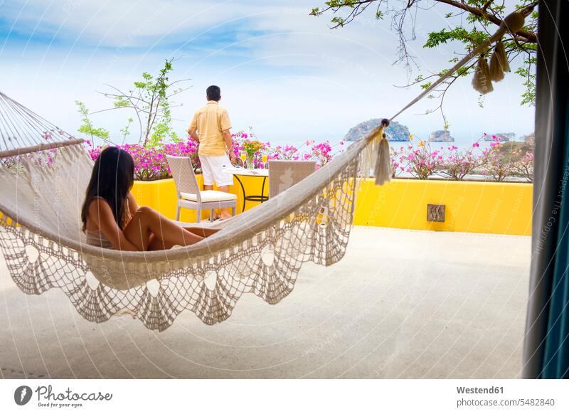 Mann und junge Frau in Hängematte auf der Terrasse Ferien Urlaub Tourismus entspannt entspanntheit relaxt Hängematten Reise Travel Entspannung relaxen