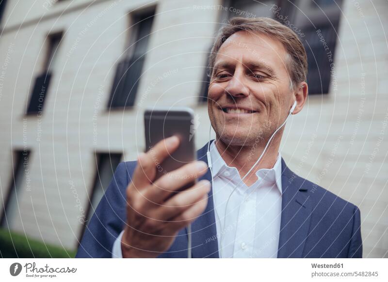 Porträt eines lächelnden reifen Geschäftsmannes im Freien mit Kopfhörern und Smartphone Handy Mobiltelefon Handies Handys Mobiltelefone Businessmann