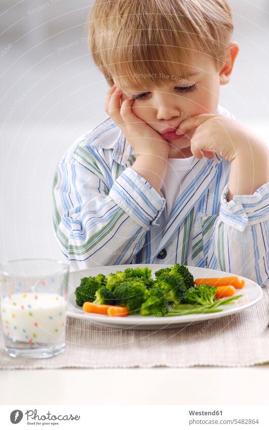 Porträt eines kleinen blonden Jungen, der auf einen Teller mit Gemüse schaut Glas Trinkgläser Gläser Trinkglas Freizeitkleidung casual Freizeitbekleidung