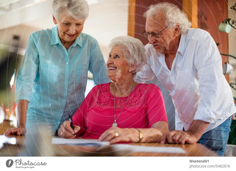 Ältere Frau unterzeichnet einen Vertrag, Freunde beruhigen sie Formular Formulare Seniorin älter Seniorinnen alt Freundschaft Kameradschaft ausfüllen ausfuellen
