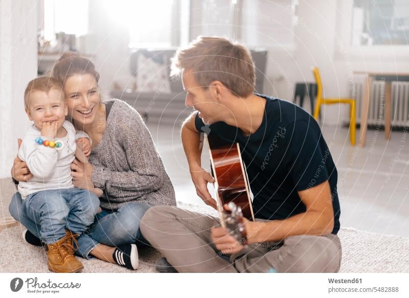 Glückliche Familie sitzt auf dem Boden, während der Vater Gitarre spielt Böden Boeden Papas Väter Vati Vatis Papis Familien sitzen sitzend glücklich