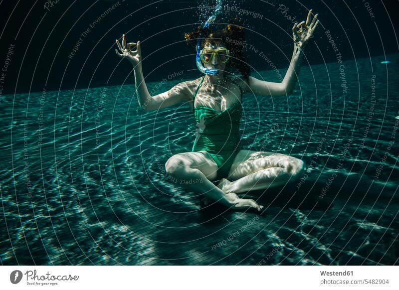 Frau mit Taucherbrille und Schnorchel sitzt in Yoga-Pose unter Wasser in einem Schwimmbad weiblich Frauen Swimmingpool Swimmingpools Schwimmbecken Swimming Pool