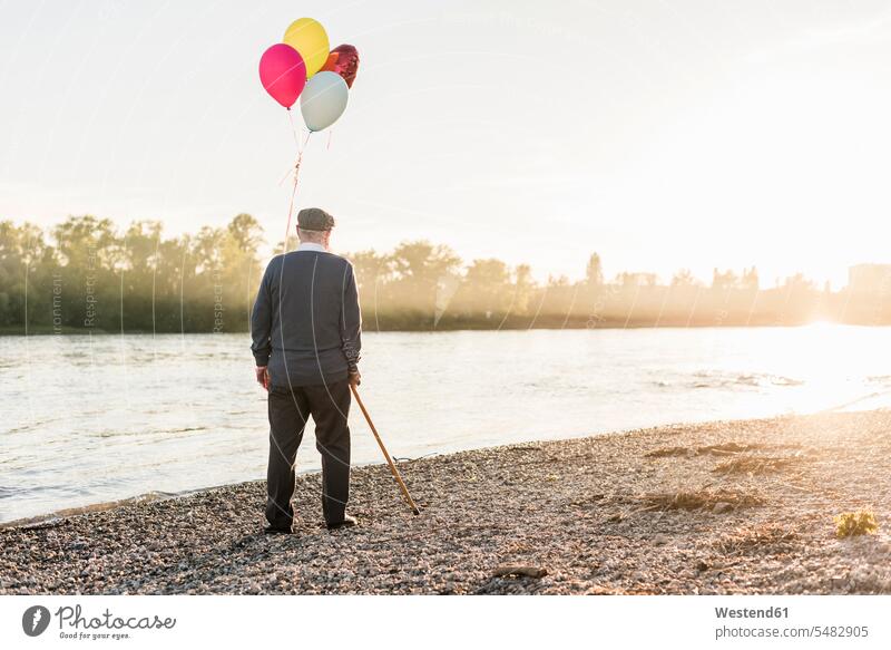 Rückenansicht eines älteren Mannes mit Luftballons, der abends am Flussufer steht Ballons Luftballone Senior ältere Männer älterer Mann Senioren männlich