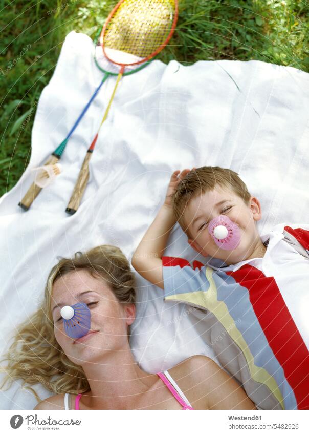 Porträt einer lächelnden Mutter und eines kleinen Sohnes mit Federbällen auf der Nase, die auf einer Decke liegen Federball Federbaelle Söhne Mami Mutti Mütter