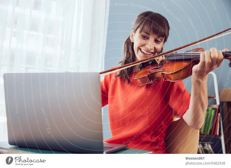 Frau benutzt Laptop, um ein Lied auf einer Geige zu spielen Violine Geigen Violinen üben ausüben Übung trainieren Notebook Laptops Notebooks lächeln weiblich