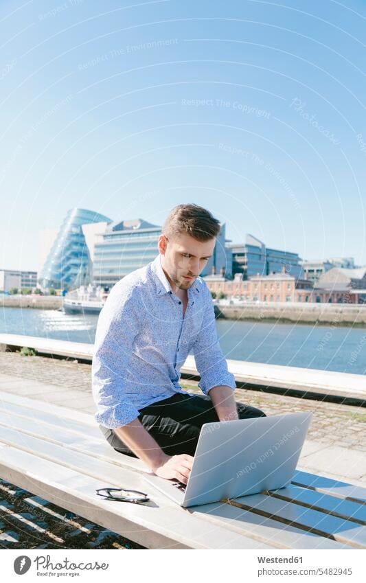 Irland, Dublin, junger Geschäftsmann sitzt mit Laptop auf der Bank Businessmann Businessmänner Geschäftsmänner Notebook Laptops Notebooks Geschäftsleute