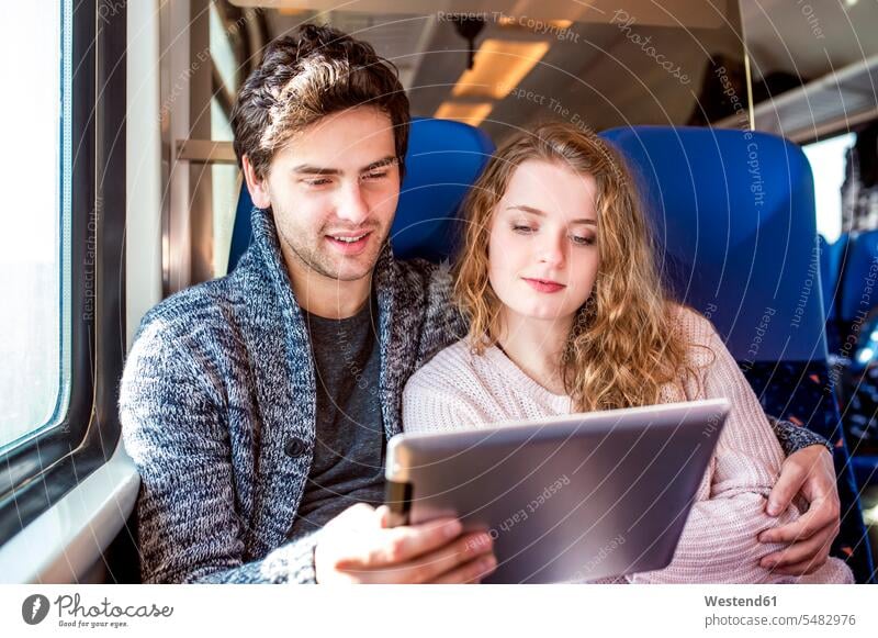 Lächelndes junges Paar im Zugwaggon mit digitalem Tablet Bahnen Züge Reise Travel sitzen sitzend sitzt Bahnreise Zugfahrt Bahnfahrt Zugreise Bahn fahren