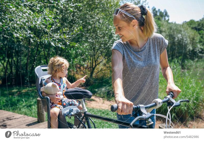 Mutter fährt mit ihrer Tochter im Kindersitz mit dem Fahrrad durch die Landschaft Mami Mutti Mütter Mama Töchter Bikes Fahrräder Räder Rad Eltern Familie