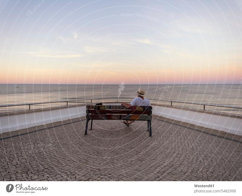 Portugal, Älterer Mann sitzt auf einer Bank und beobachtet den Sonnenaufgang Männer männlich Strand Beach Straende Strände Beaches Tourist Touristen Sitzbänke