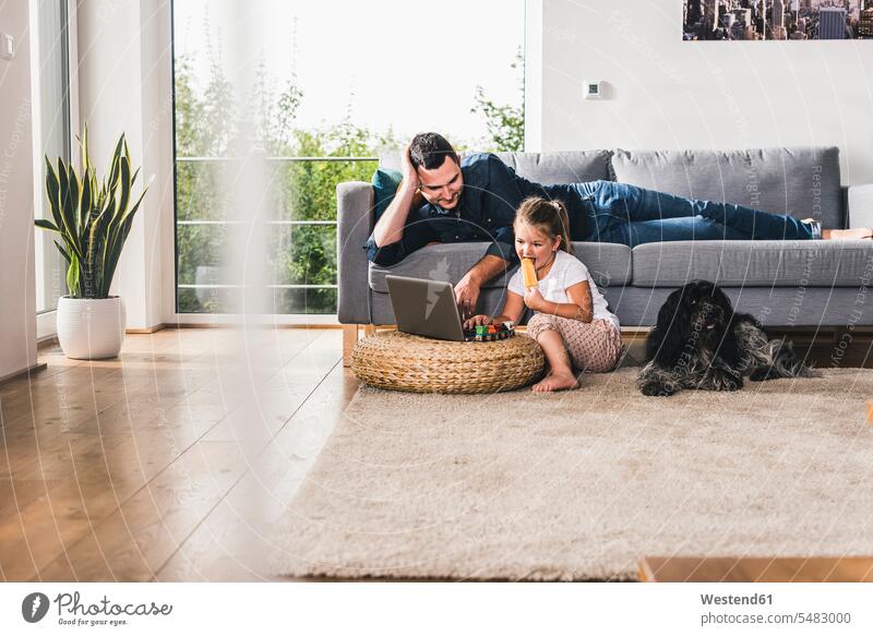 Vater benutzt Laptop zu Hause mit seiner kleinen Tochter Hund Hunde Zuhause daheim Papas Väter Vati Vatis Papis lernen Notebook Laptops Notebooks Töchter