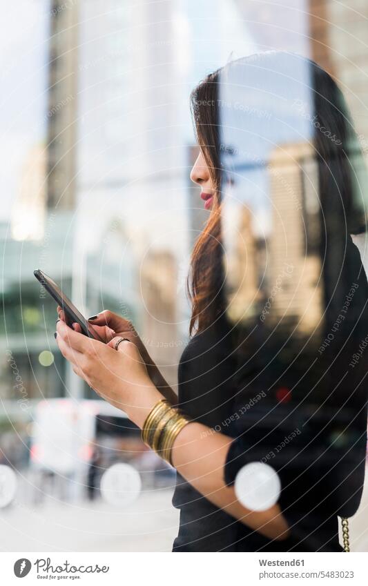 USA, New York City, Manhattan, junge Frau hinter Glasscheibe mit Blick auf Mobiltelefon weiblich Frauen Smartphone iPhone Smartphones Erwachsener erwachsen