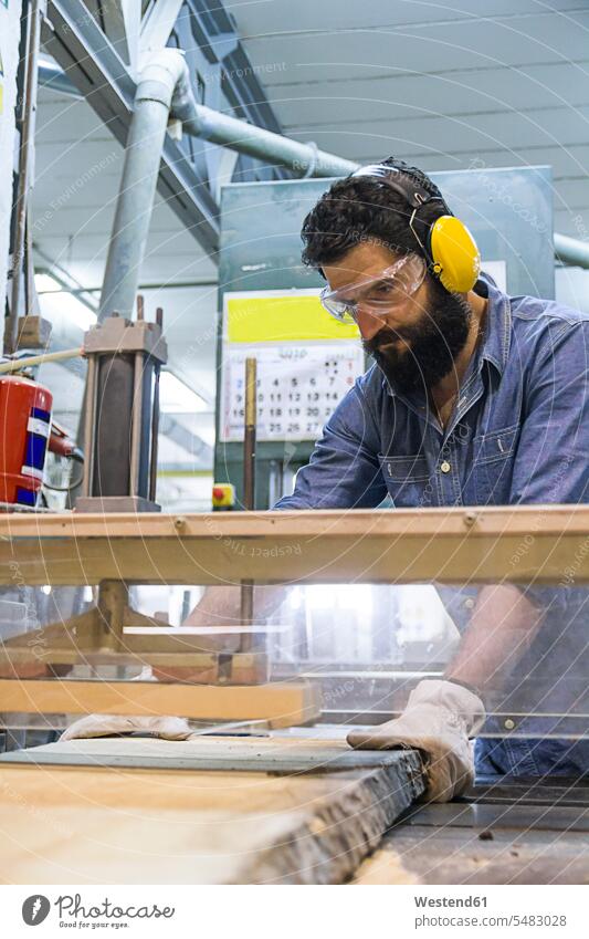 Handwerker mit Gehörschutz, Handschuhen und Schutzbrille an einer Industriekreissäge in einer Fabrik Brett Bretter Sägewerk Saegewerke Schneidemuehle Sägemühle