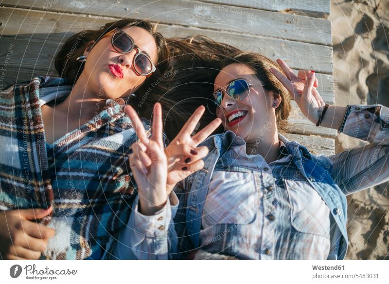 Zwei junge Frauen liegen auf Holzbrettern und zeigen Siegeszeichen Freundinnen liegend liegt Freunde Freundschaft Kameradschaft Portrait Porträts Portraits