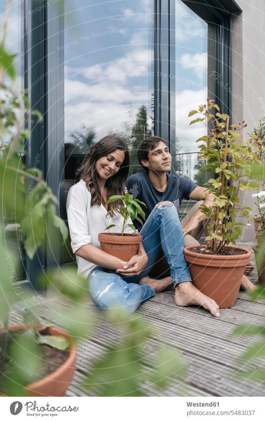 Glückliches Paar mit Pflanzen, die sich auf dem Balkon entspannen Balkone entspannt entspanntheit relaxt lächeln Pärchen Paare Partnerschaft sitzen sitzend