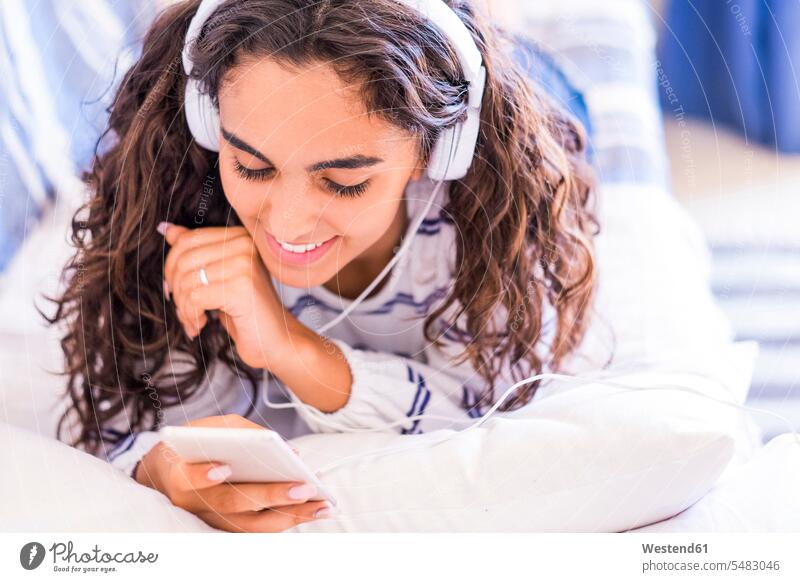 Lächelndes Teenager-Mädchen liegt mit Smartphone und Kopfhörern auf der Couch Kopfhoerer Teenagerin junges Mädchen Teenagerinnen weiblich junge Frau Sofa